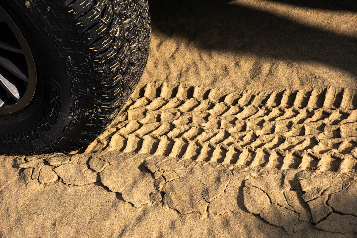 An off-road tyre beside its own deep track pressed into dry sand